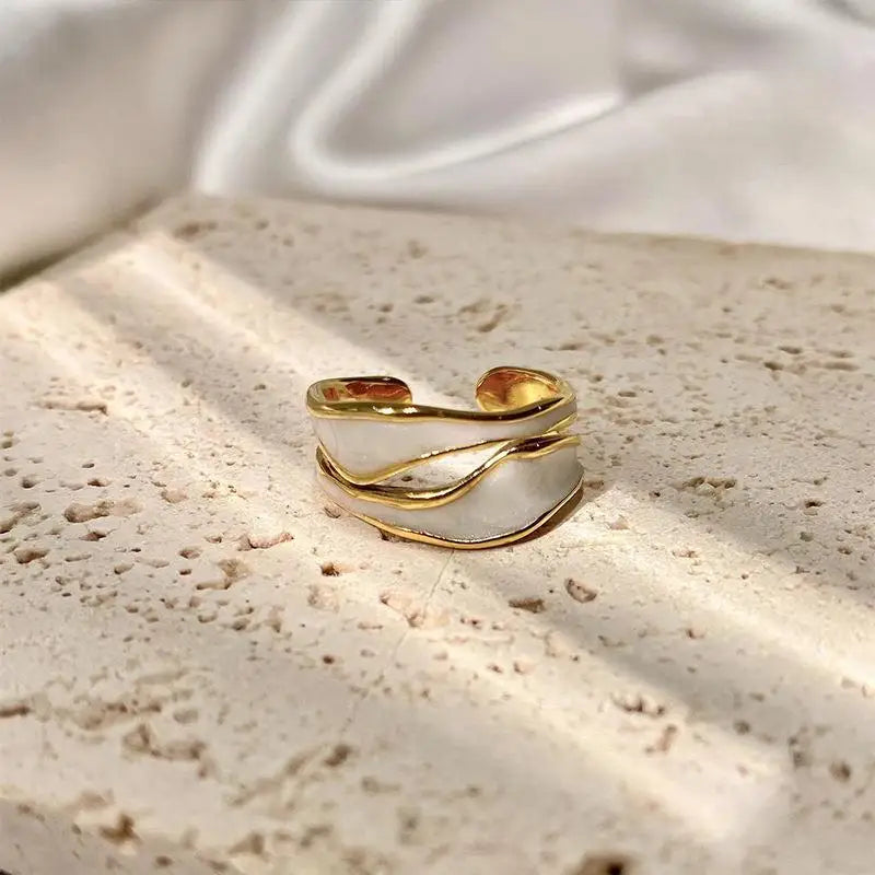 Retro gold open ring with white enamel wavy design displayed on a textured stone surface