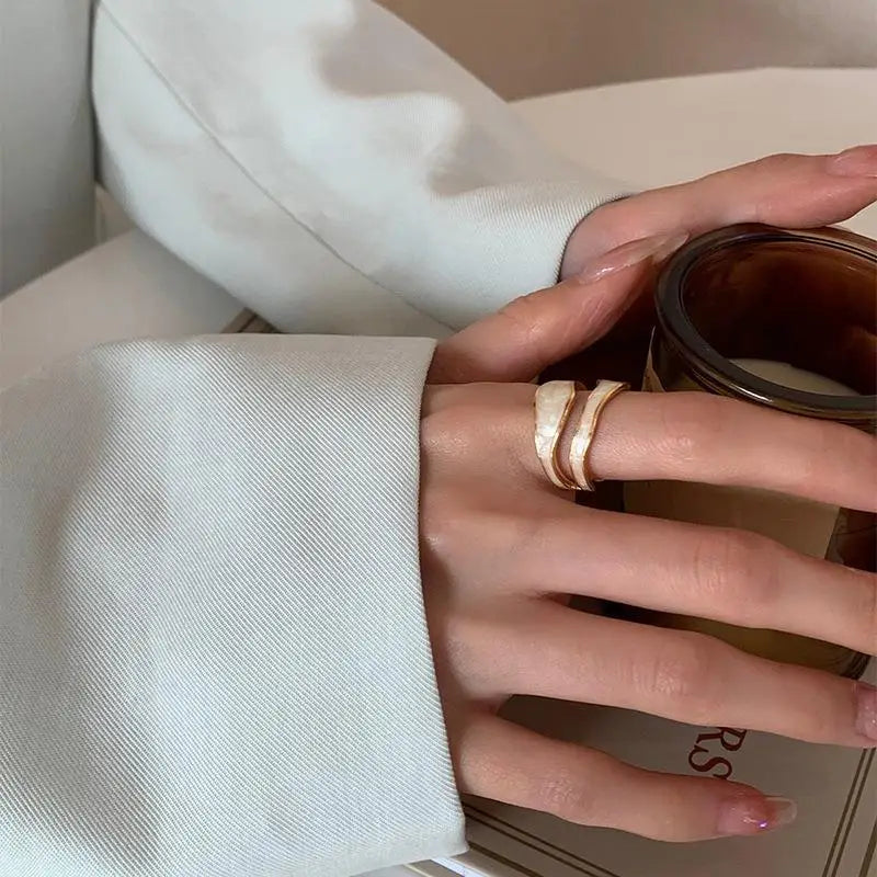 Close-up of a retro gold open ring with white enamel worn on a woman’s hand while holding a coffee cup