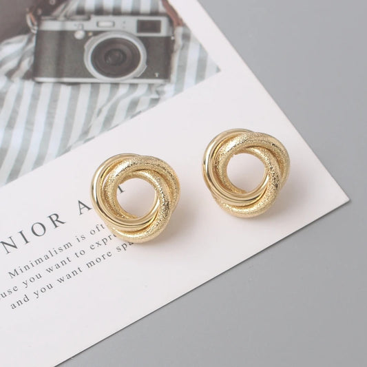 Pair of gold swirl statement earrings displayed on a card with a camera design background